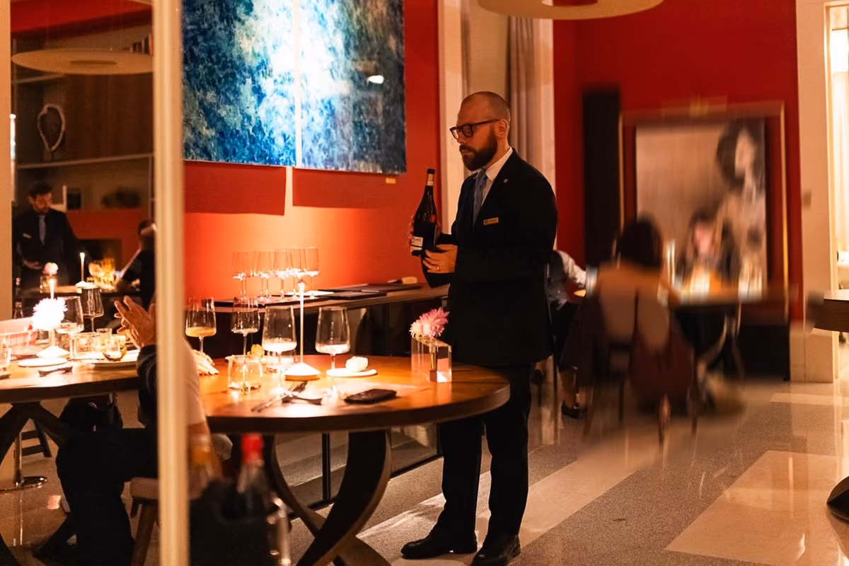 sommelier in abito elegante serve vino al tavolo in una sala ristorante