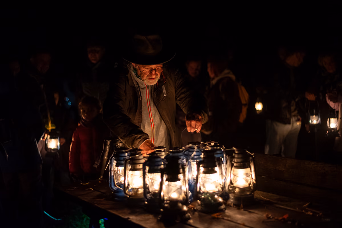 uomo anziano con cappello accende lanterne a olio in un bosco notturno