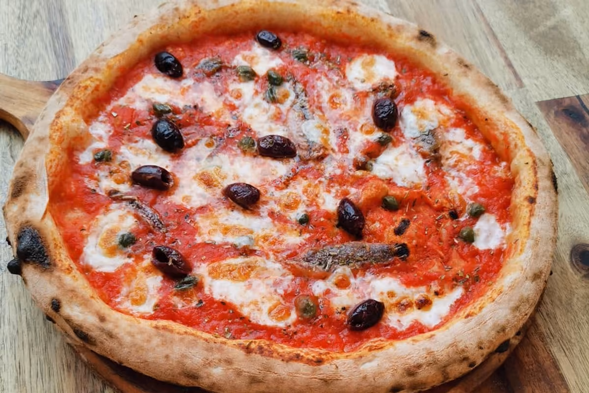pizza napoletana con pomodoro mozzarella olive nere acciughe e capperi su tagliere in legno