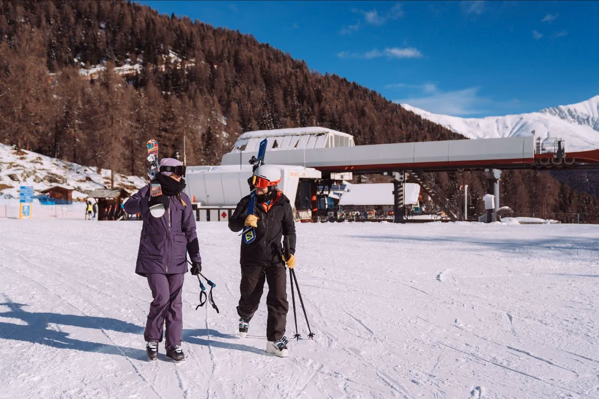 Due sciatori con attrezzatura in spalla camminano su una pista innevata in montagna