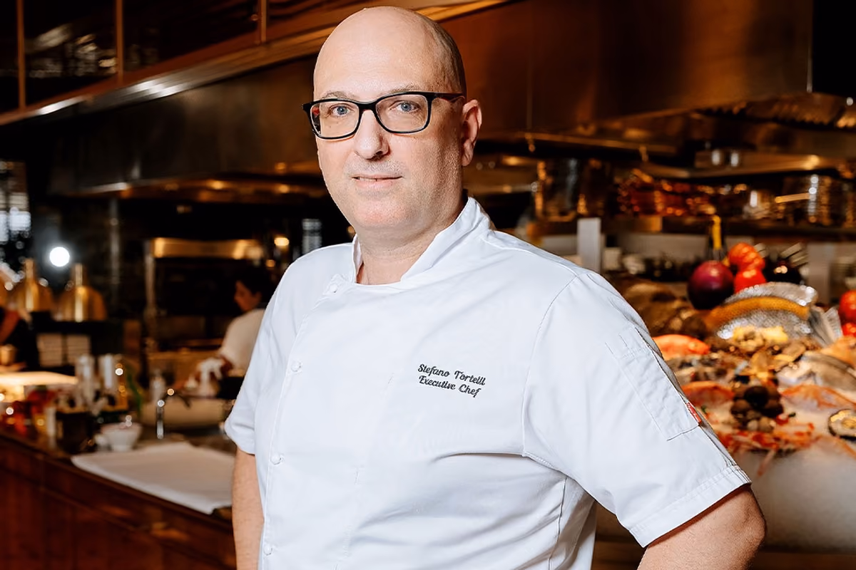 Lo chef Stefano Tortelli in divisa bianca professionale all'interno di una cucina