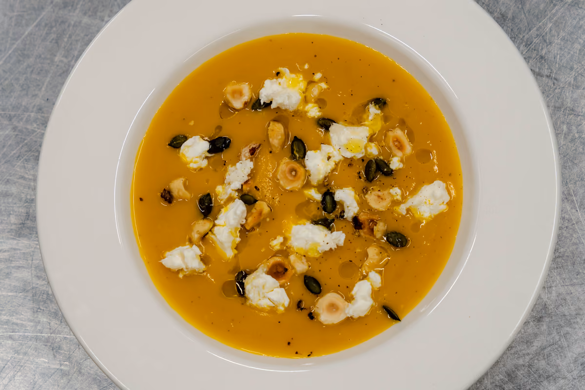 zuppa arancione guarnita con formaggio fresco, nocciole e semi di zucca nel piatto