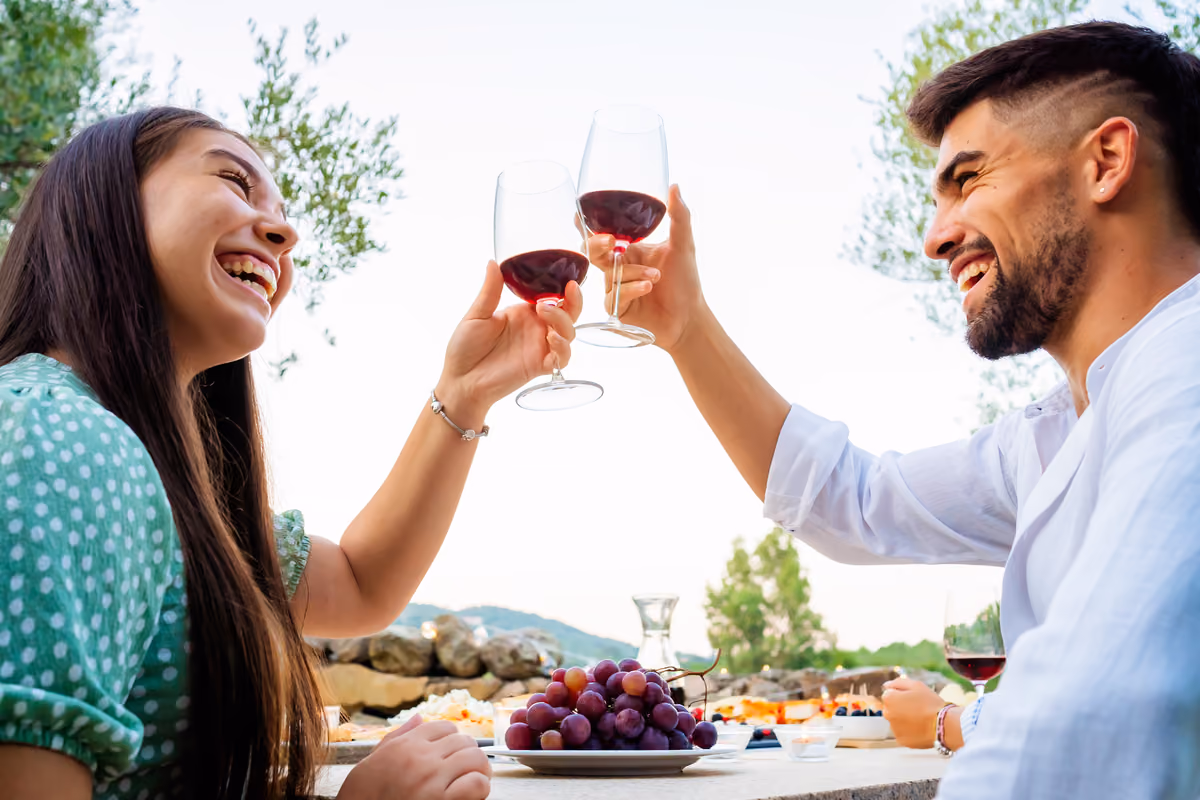 Coppia che brinda con vino rosso davanti a un piatto di uva