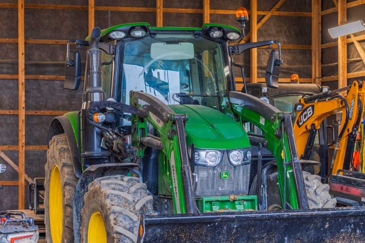 trattore verde John Deere parcheggiato in un capannone agricolo con macchinari pesanti