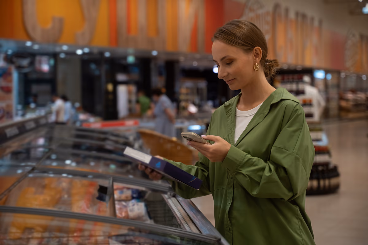 giovane donna che consulta lo smartphone scegliendo prodotti surgelati al supermercato