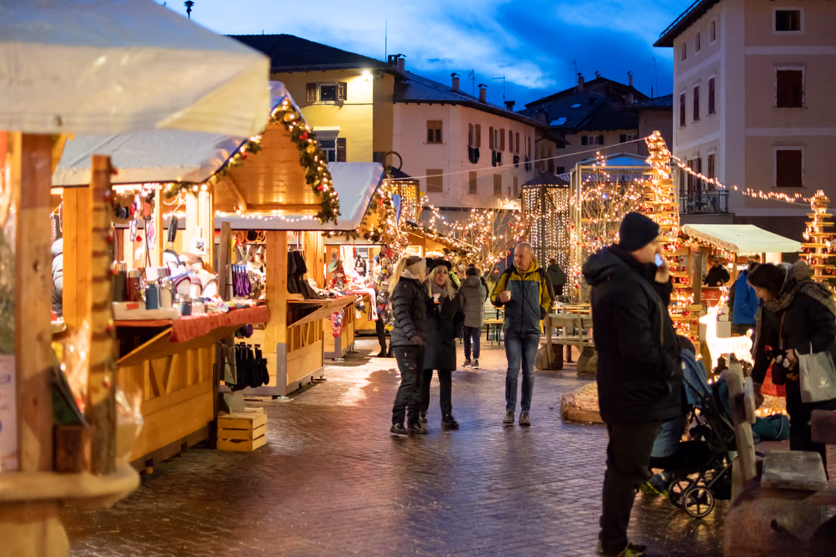 Mercatino di Natale all'aperto con bancarelle di legno illuminate e persone che passeggiano la sera