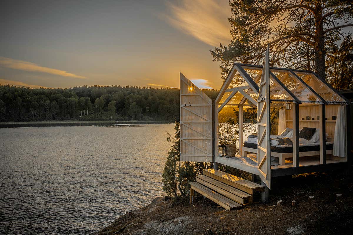 Una 72 Hour Cabin di vetro illuminata dalla luce del tramonto nella foresta del Dalsland