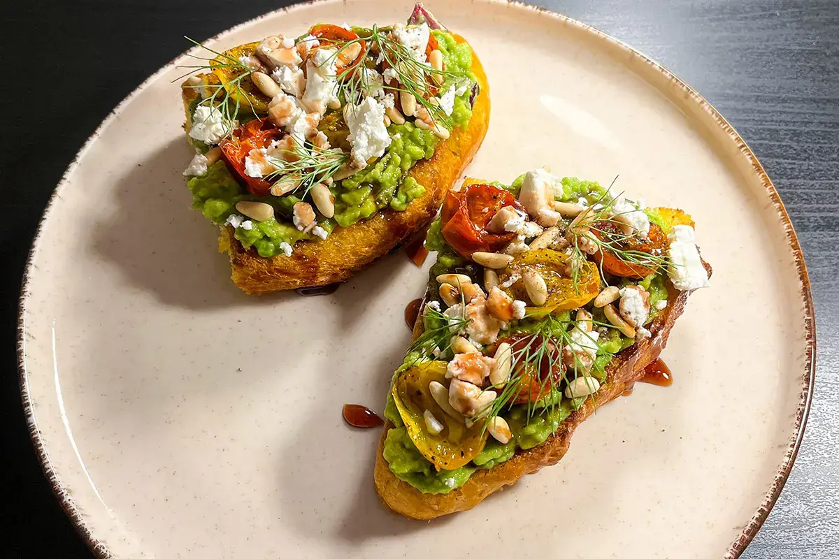 Avocado toast con feta, pinoli, pomodorini confit e sciroppo di melograno Avocado toast con feta, pinoli e pomodorini