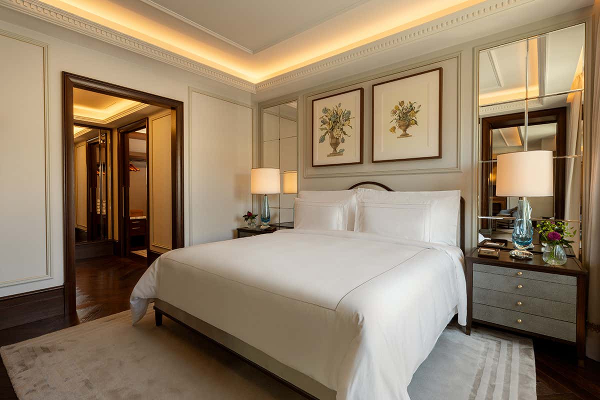 La camera da letto della Arte Suite al sesto piano di Corinthia Rome: un ambiente intimo arricchito da opere d'arte botaniche alle pareti, boiserie geometrica e lampade di design in vetro soffiato