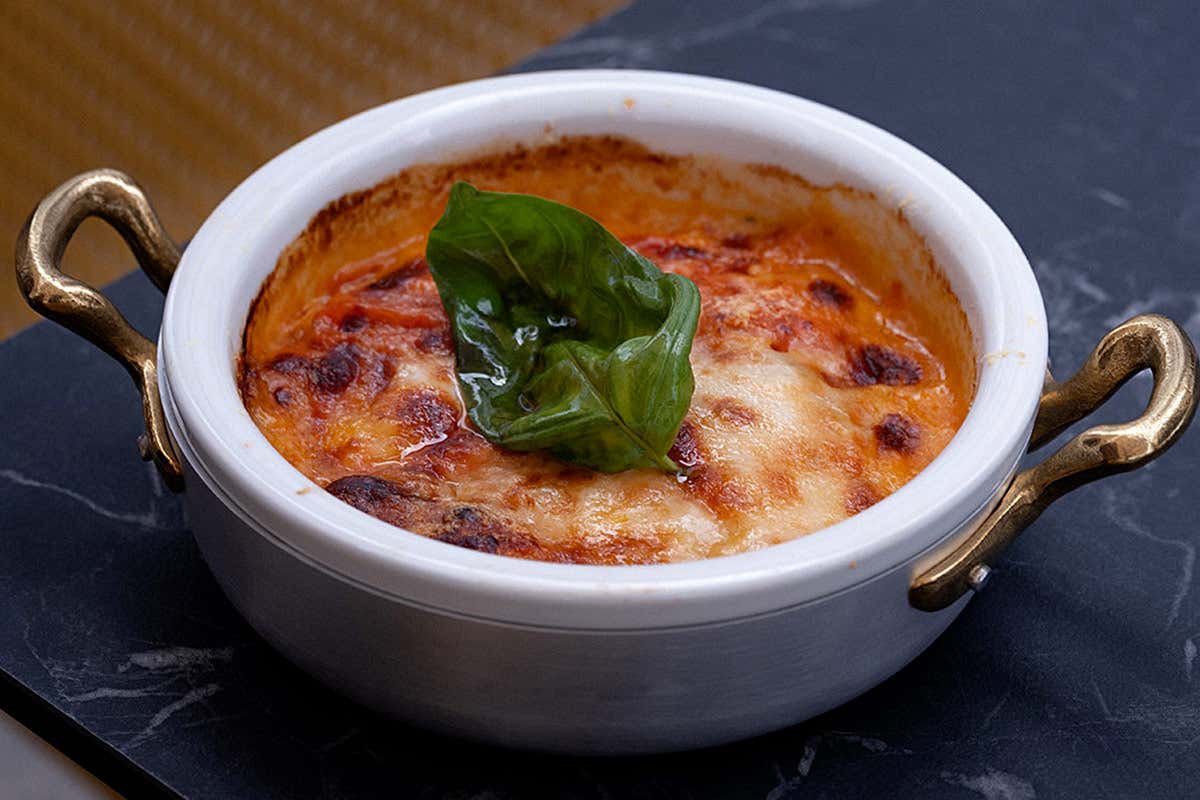 Una parmigiana di melanzane servita in un tegame singolo, guarnita con basilico fresco, un piatto che richiama la tradizione culinaria italiana