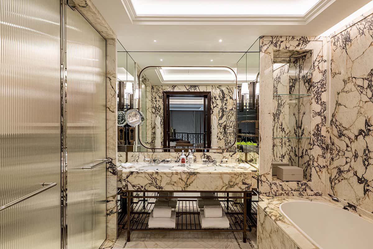 Il bagno in marmo della Campo Marzio Suite, dotato di doppia postazione lavabo, specchiature geometriche e finiture metalliche coordinate che esaltano il disegno delle venature naturali