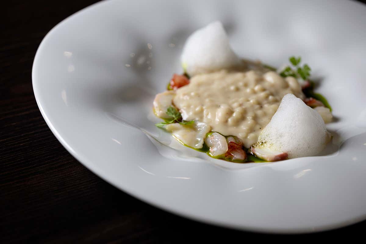 “Fagioli e abissi”, una fregola sarda tostata servita con crema di fagioli cannellini, jus di fagioli misti, crudo di crostacei, molluschi del Mediterraneo e aria di mare al limone.