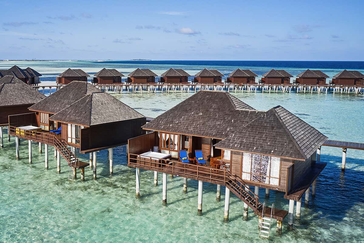 La firma maldiviana: le iconiche palafitte overwater disposte lungo i pontili sospesi sulla laguna turchese