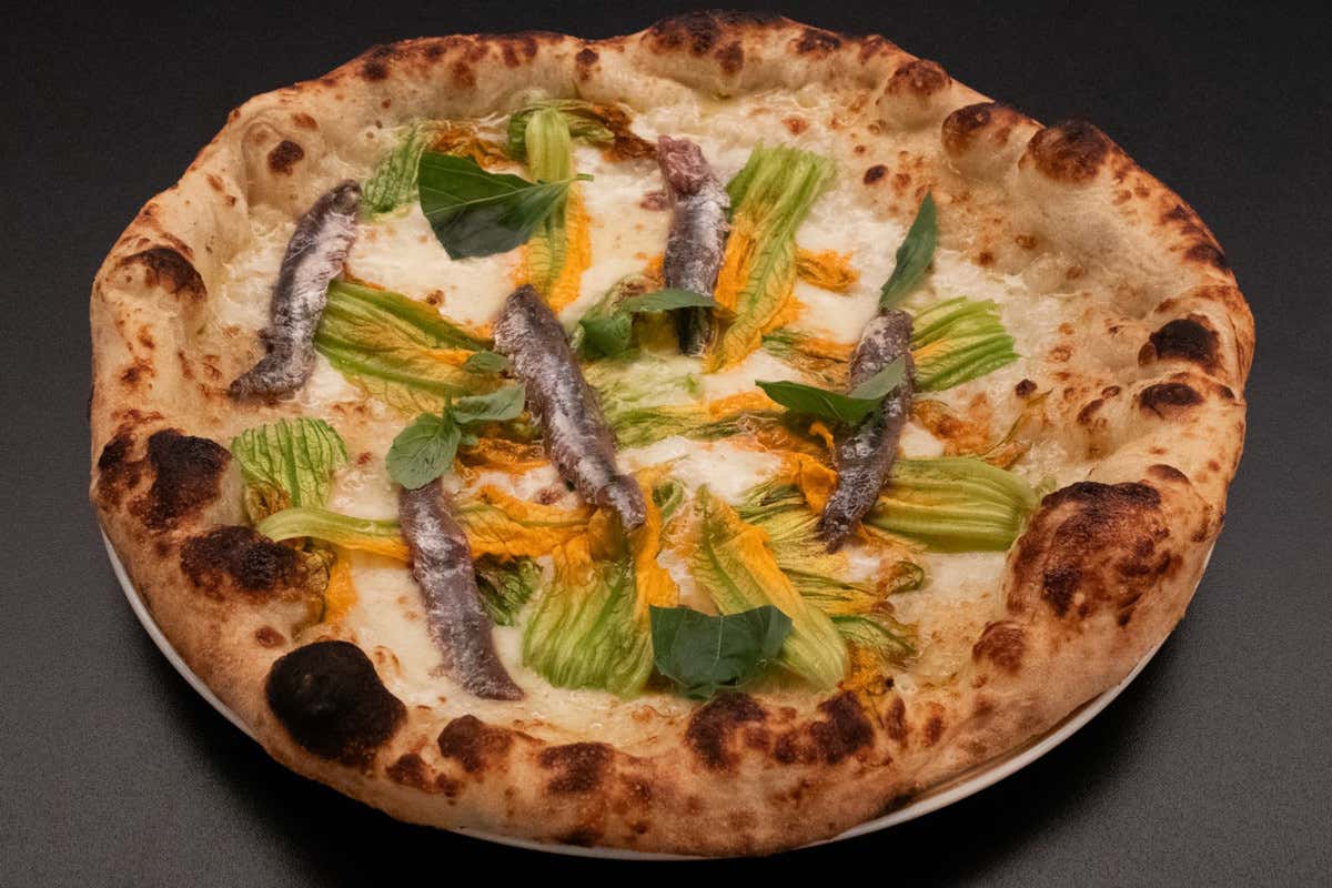 Pizza a ruota di carro, parmigiano, fior di latte e fiori di zucca, guarnita con alici di Cetara, olio e basilico