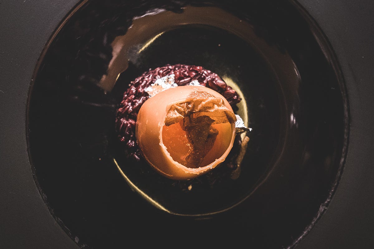 Uovo di cristallo ripieno di morbido albume, Grana Padano Dop oltre 20 mesi e patata, con il suo tuorlo su riso nero, oro e tartufo bianco “Nati per stare insieme” da Tano Passami l’Olio