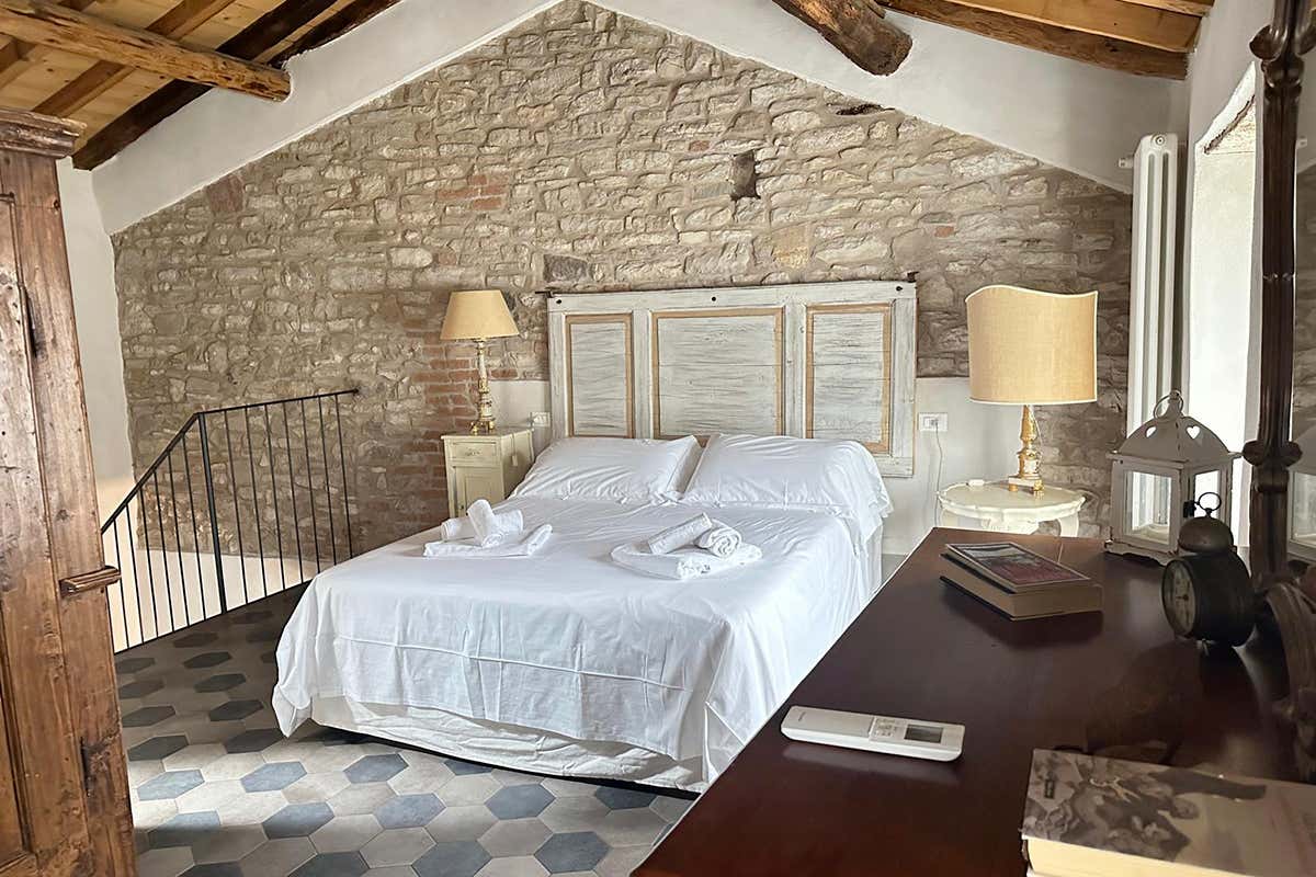 La camera da letto matrimoniale sul soppalco: un rifugio accogliente sotto il soffitto in legno, dominato dalla imponente parete in pietra originale del borgo