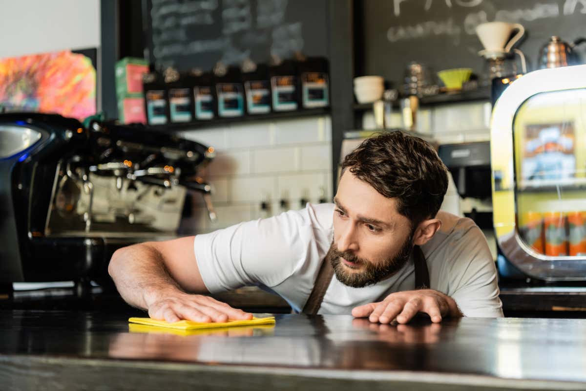 barista con barba pulisce con attenzione il bancone di un locale