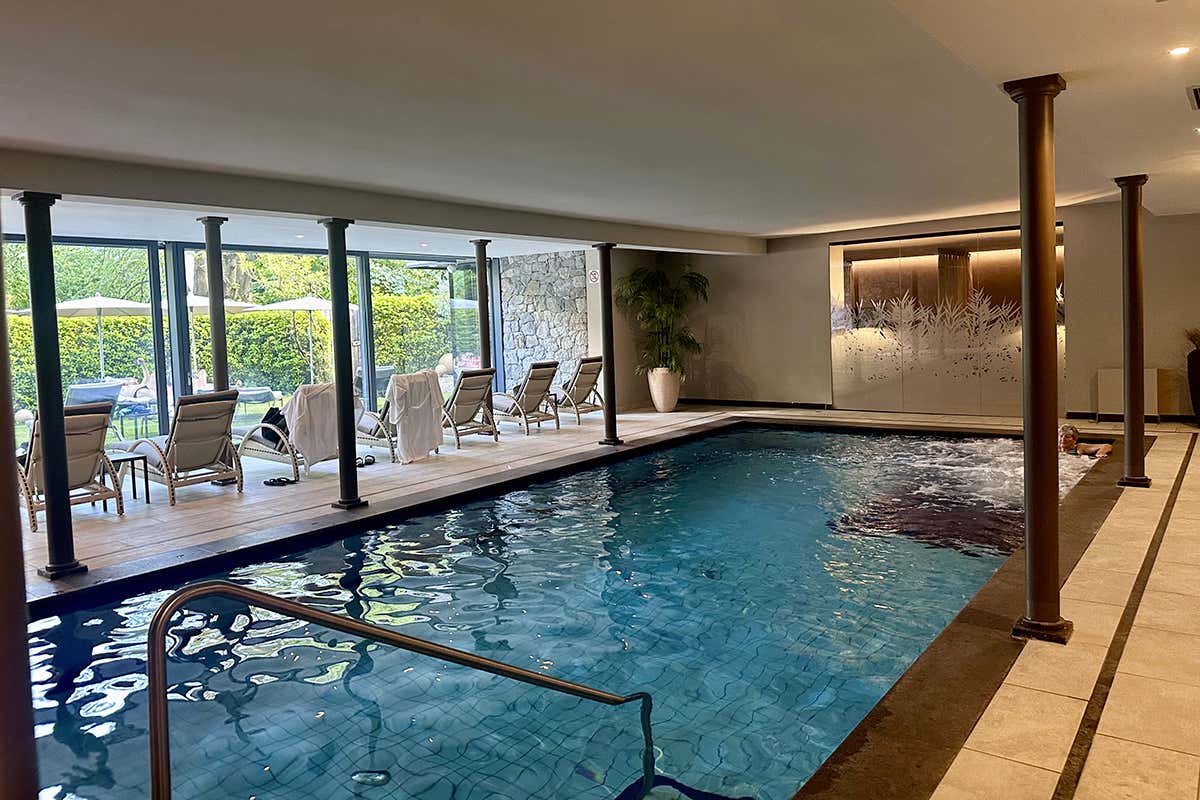 La grande piscina coperta riscaldata dell'hotel, caratterizzata da ampie vetrate che offrono un accesso diretto al giardino solarium esterno