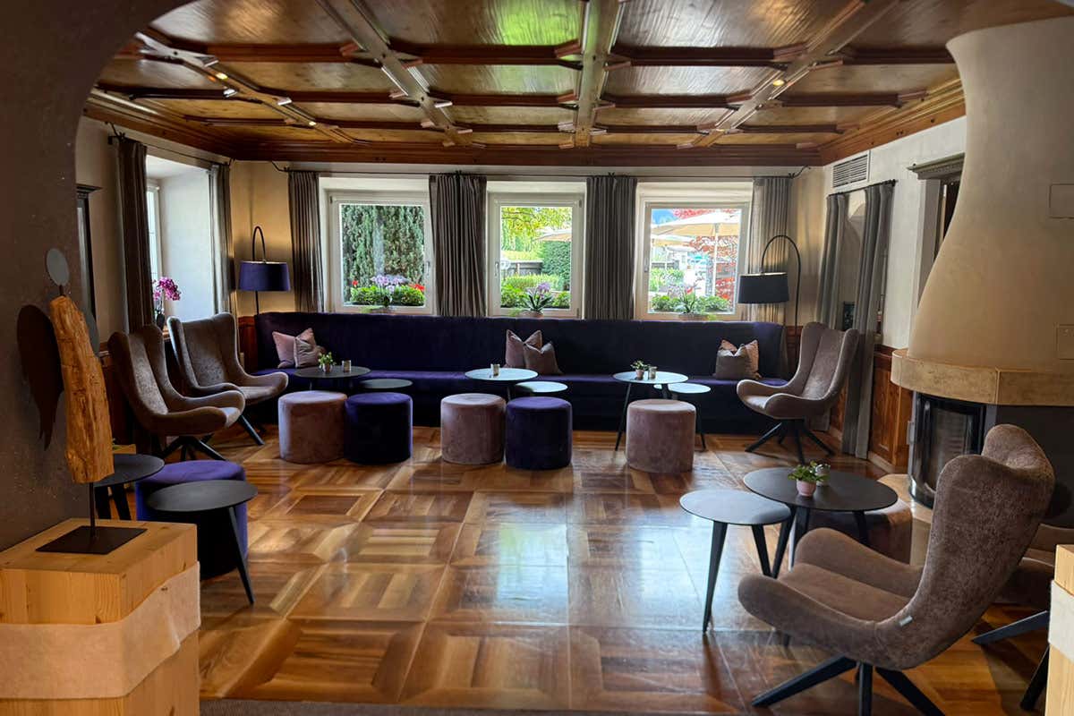 La sala comune dell'Engels Park accoglie gli ospiti in un ambiente raffinato, dove il calore del soffitto a cassettoni in legno e del caminetto si sposa con il comfort moderno di poltrone e divani in velluto