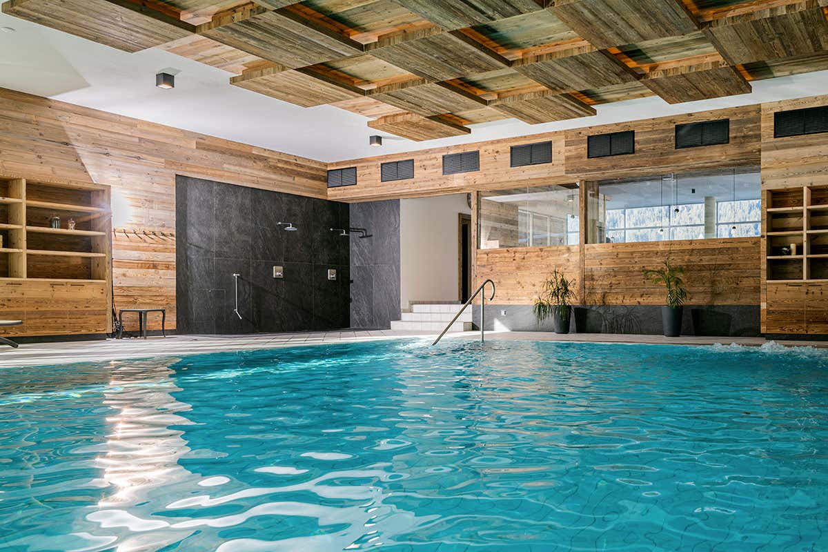La piscina interna panoramica del centro benessere, dove il design materico degli interni dialoga con la luce naturale e il profilo delle vette alpine