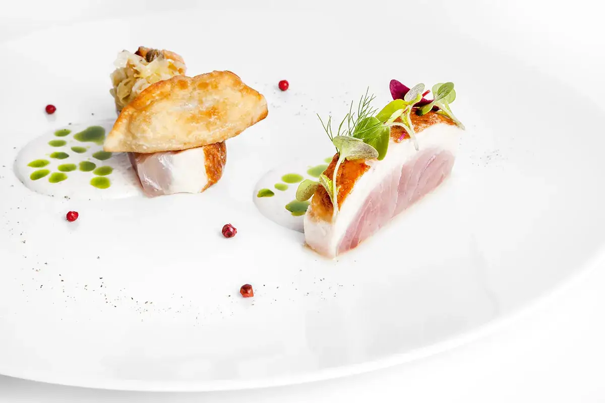Trancio di ricciola leggermente scottato poi marinato ai porri, capperi e guanciale con raviolo croccante di ostrica e salsa di merluzzo Trancio di ricciola con raviolo croccante di ostrica e salsa di merluzzo