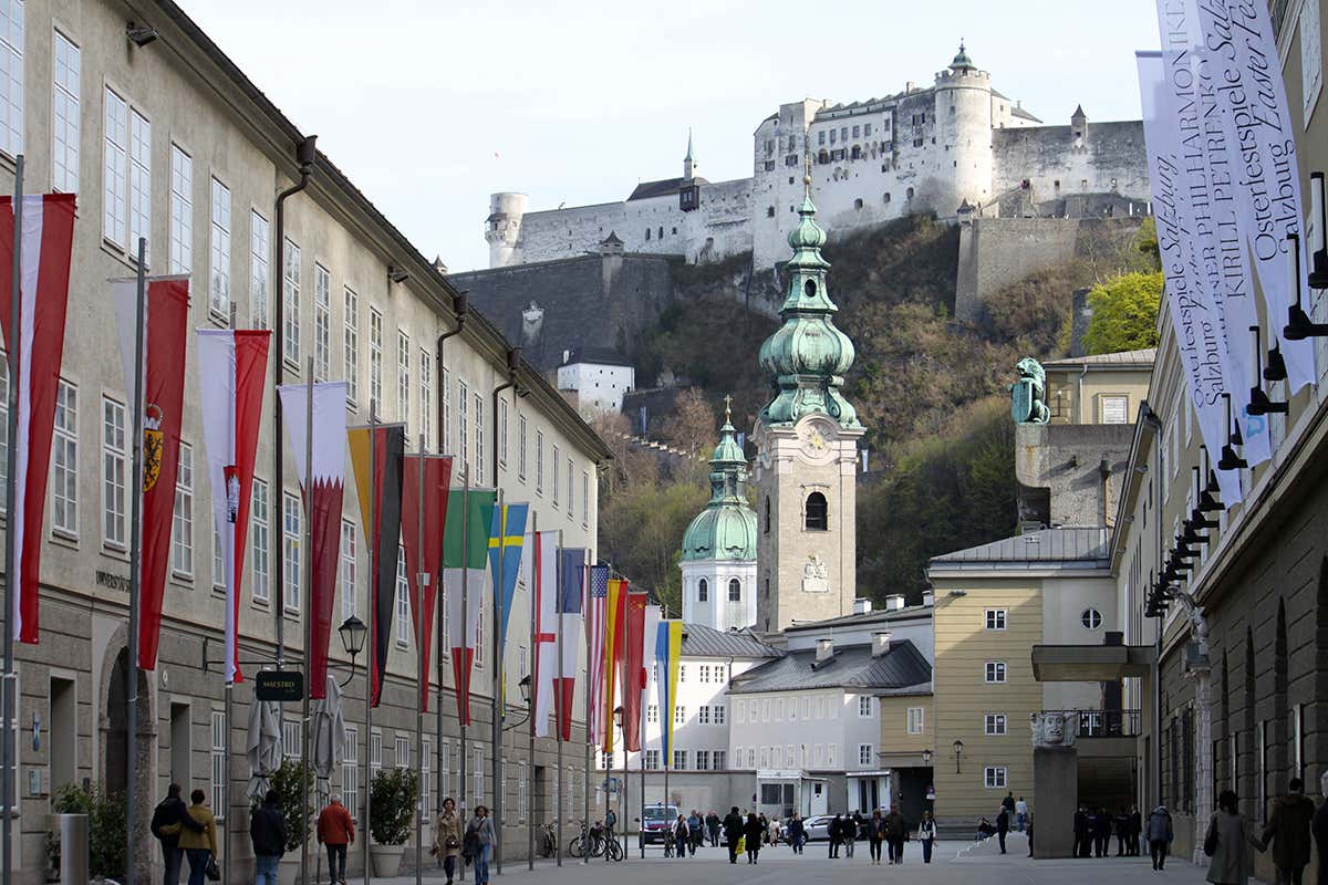 Nel cuore del quartiere dei festival, la Hofstallgasse conduce tra bandiere internazionali verso la Fortezza di Hohensalzburg e il centro storico di Salisburgo