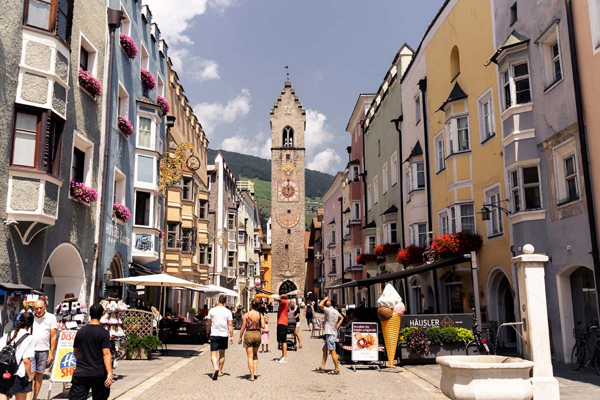 Passeggiando lungo il corso di Città Nuova a Vipiteno: le caratteristiche facciate colorate con i tipici bovindi incorniciano la vista verso la maestosa Torre delle Dodici