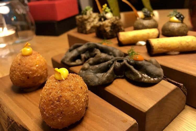 Arancino di riso, maionese all’arancia e fiore di tagete; Chiacchiere al nero di seppia con crema di peperone e finocchietto selvatico (I segreti più intimi del gardesano 
in tavola al Ristorante Alle Rose di Salò)